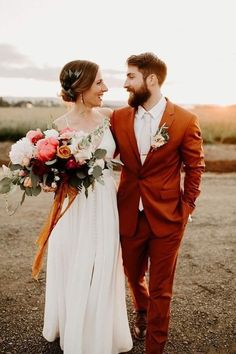 a bride and groom are walking together in the desert with flowers on their bouquets