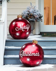 two red christmas baubles sitting on the front steps of a house with merry written on them