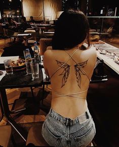 a woman sitting at a table with her back turned to the camera and tattoos on her body