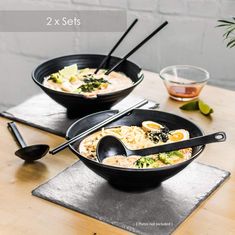 two black bowls filled with food on top of a wooden table