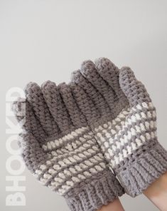 a woman's hand holding up a gray and white knitted mitt