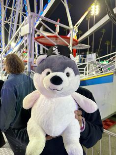 a man holding a white and gray teddy bear in front of a ferris wheel at night