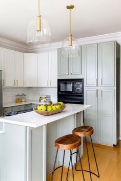 a kitchen with two stools in front of an island and some fruit on the counter