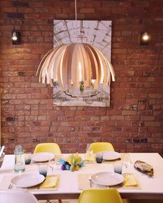 a dining room table with yellow chairs and plates on it, in front of a brick wall