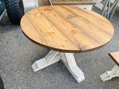 a wooden table sitting on top of a cement ground next to a motorcycle tire and some chairs