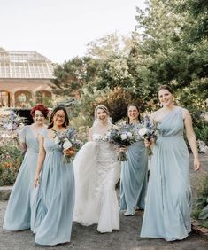 a group of women standing next to each other in front of trees and flowers on the ground