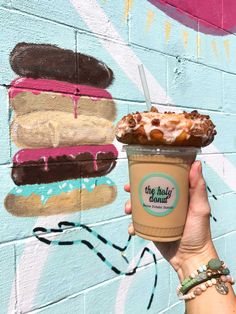 a hand holding up a cup of ice cream and a doughnut on the side of a building