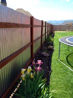 a fenced in yard with flowers and a trampoline on the grass next to it