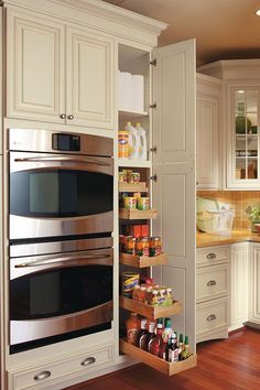 an open pantry in the middle of a kitchen with white cabinets and wood flooring