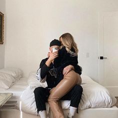 a man and woman sitting on top of a bed taking pictures with their cell phones