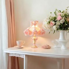 a white table topped with a lamp next to a vase filled with pink and white flowers