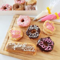 a wooden cutting board topped with donuts covered in frosting and happy new year lettering