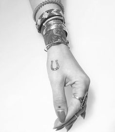 a woman's hand with a horseshoe tattoo on her left thumb and bracelets around her wrist