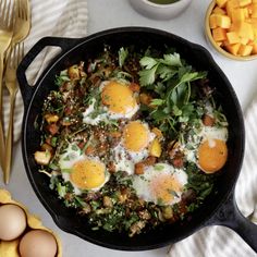 a skillet filled with eggs and greens on top of a table next to other food