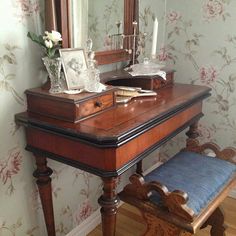 a wooden desk with a mirror, bench and flowers on it in front of a floral wallpapered wall