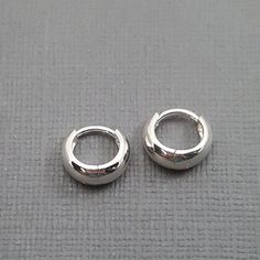 two small silver hoop earrings sitting on top of a gray cloth covered tablecloth,