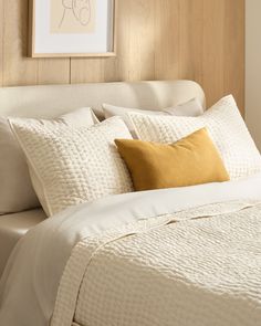 a white bed topped with lots of pillows next to a framed picture on the wall