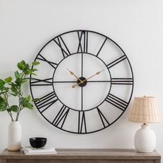 a clock on the wall next to a table with a lamp and potted plant