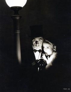 a man and woman standing next to each other under a street light with a lamp in the background