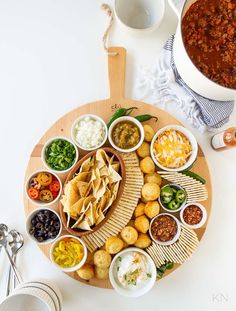 a platter filled with tacos, salsa and tortilla chips next to a pot of chili