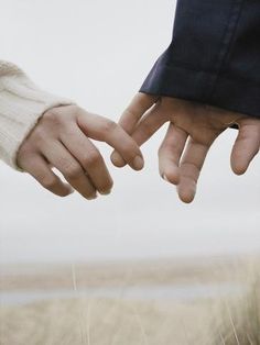 two people holding hands in front of the ocean and sand on the beach, with one person's hand reaching for the other