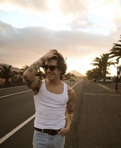 a man with tattoos and sunglasses standing in the middle of an empty street at sunset