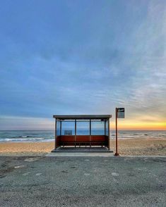 a bus stop sitting on top of a sandy beach next to the ocean at sunset