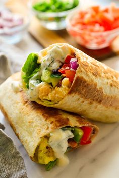 two burritos are sitting on a plate with some salad in the middle and one is cut in half