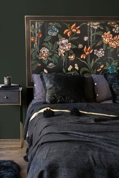 a bed with black linens and flowers on the headboard is next to a night stand