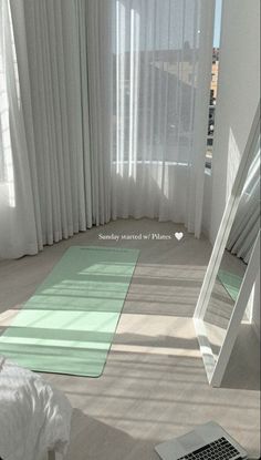 a room with white curtains and green rugs on the floor next to a laptop