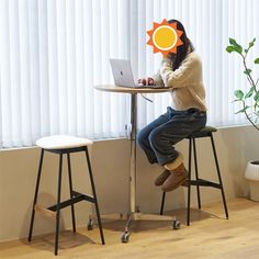 a woman sitting at a table with a laptop computer in front of her, holding an orange sun cutout above her head