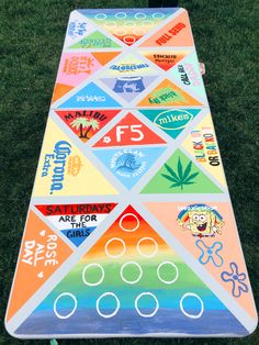 a colorful cornhole board sitting on top of the grass with stickers all over it