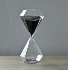 an hourglass sitting on top of a wooden table next to a vase filled with black sand