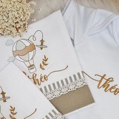 three white onesuits with embroidered designs on them and some dried flowers in the background