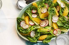 a salad with radishes and oranges in a bowl on a table next to silverware