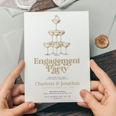 two hands holding up a card with champagne glasses on it and the words engagement party written in gold