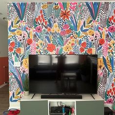 a flat screen tv sitting on top of a white entertainment center in front of a colorful wall