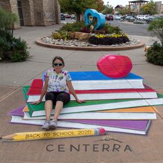 a woman sitting on top of a giant pile of books in front of a building