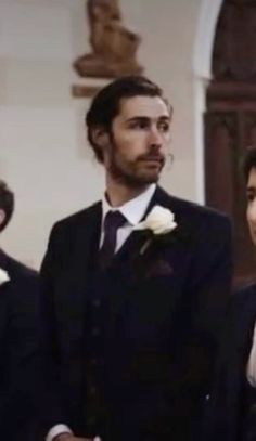 two men in tuxedos standing next to each other and one man wearing a suit