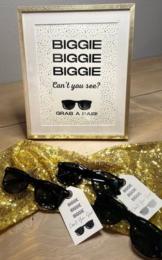 two pairs of sunglasses sitting on top of a table next to a sign that says, biggie biagie can't you see? grab a pair