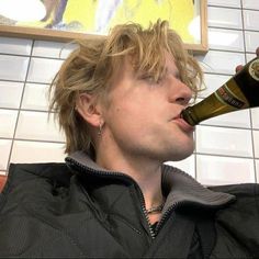 a man drinking beer from a bottle in front of a painting on a white tile wall