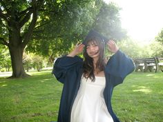 a woman wearing a graduation cap and gown in the grass with her hands on her head