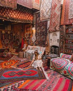 a woman sitting on top of a colorful rug in a room filled with couches and rugs