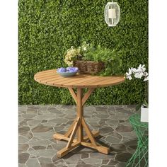 a wooden table sitting on top of a stone floor next to a green hedge wall