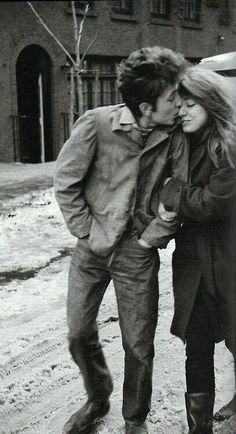 black and white photograph of two people walking in the snow, one kissing the other