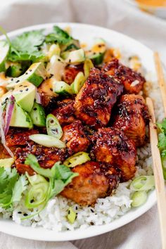 a white plate topped with chicken and rice next to chopsticks on a table