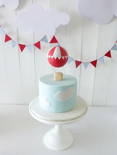 a blue cake with an air balloon on top is sitting on a white pedestal in front of red and blue bunting