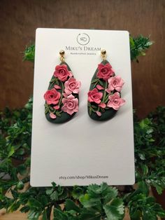 a pair of earrings with pink flowers on them sitting on top of a card board