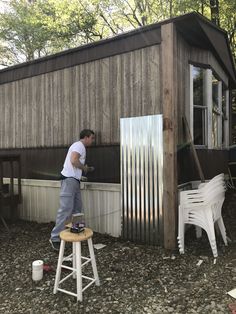 a man standing on top of a stool next to a wooden building with a metal door