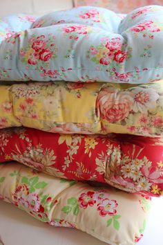 a stack of pillows sitting on top of a white table next to a vase filled with flowers